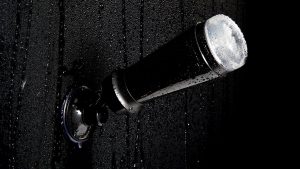 a fleshlight masturbator in a black case fixed to wet black tiles with a suction cup shower mount
